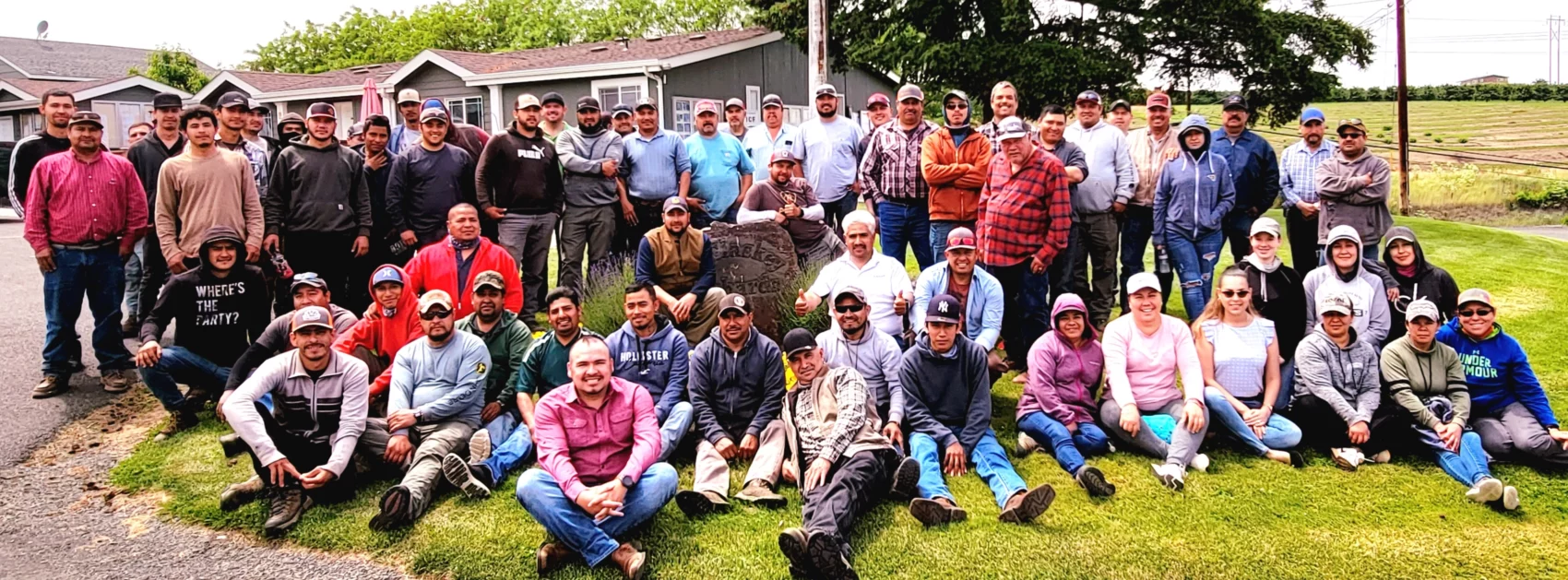 Group photo of staff or workers at McClaskey Orchards from 2022 sitting and standing on grass with an office or house behind them.